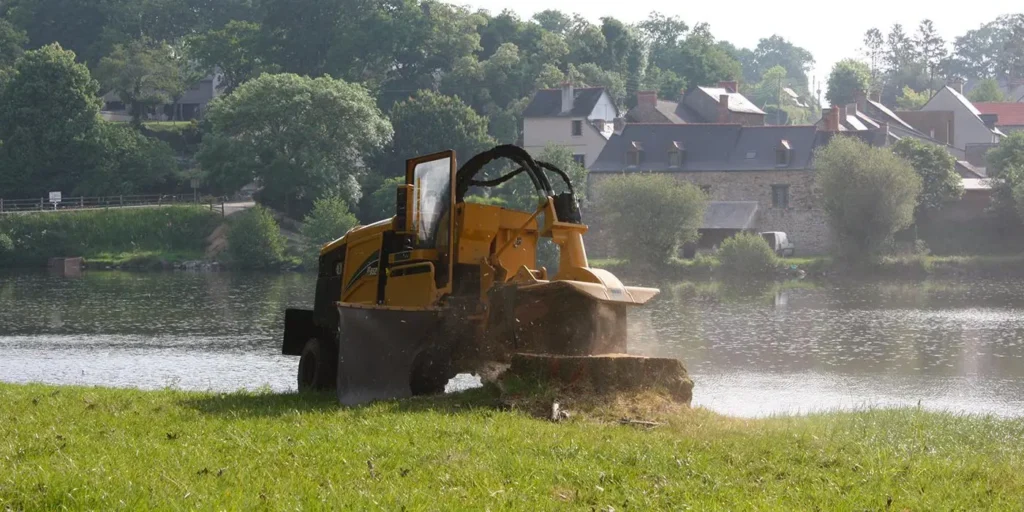Rogneuse de souche jaune éliminant une souche d'arbre au bord rivière